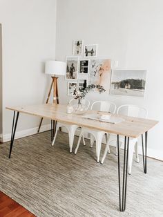 a wooden table with white chairs and pictures on the wall behind it in a living room