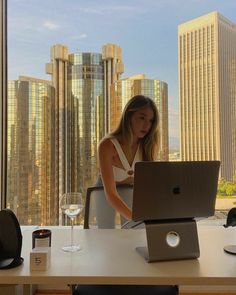 a woman sitting in front of a laptop computer on top of a desk next to a window