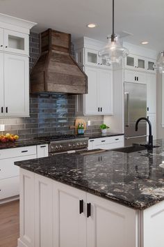 a kitchen with marble counter tops and white cabinets, an island in the middle is surrounded by hanging lights