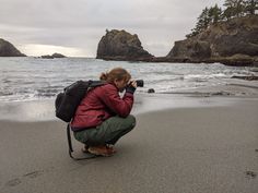 a woman kneeling down to take a photo on the beach with her camera in hand