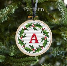 a cross stitch christmas ornament hanging from a tree with the letter a on it