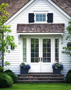 a white house with black shutters and two planters on the front steps,