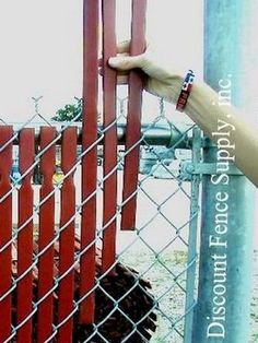 a hand is holding onto a chain link fence with dirt in the ground behind it