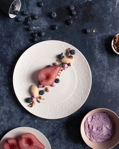 two plates with desserts on them sitting next to bowls of blueberries and granola