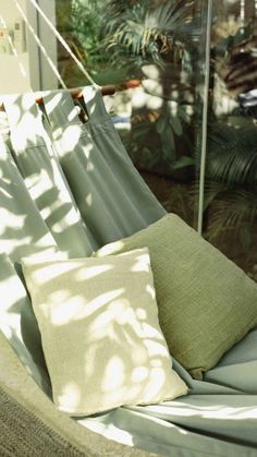 a hammock with two pillows on it in front of a glass wall and palm trees