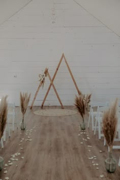 an indoor wedding setup with white chairs and flowers on the floor in front of a wall