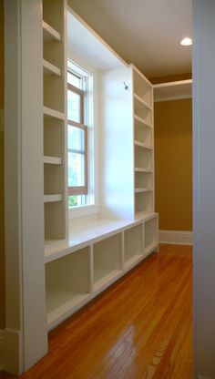 an empty room with white shelving and wood flooring in front of a window