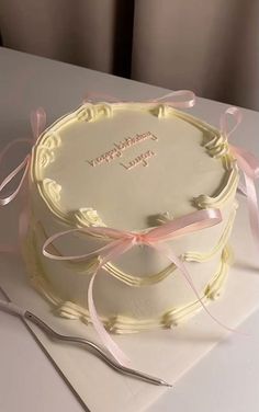 a white cake with pink ribbon on top and a knife next to it, sitting on a table