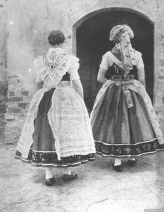 two women in long dresses are standing by an open door and looking at the ground