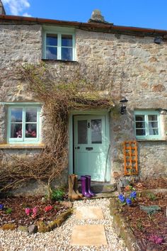 an old stone house with green doors and window frames on the outside, surrounded by plants and flowers