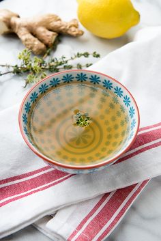 a bowl filled with liquid sitting on top of a table next to lemons and ginger