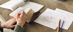 a person sitting at a table with an open book and pencils in their hands