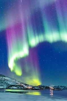 the northern lights shine brightly in the night sky over water and snow covered mountains,