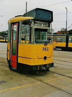 a yellow trolley sitting on the side of a road next to another train and some wires