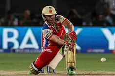 a cricket player in red and white is hitting the ball with his bat as he stands behind him