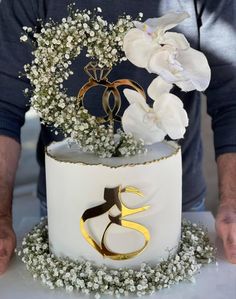 a man is holding a cake decorated with flowers and two rings on it's side