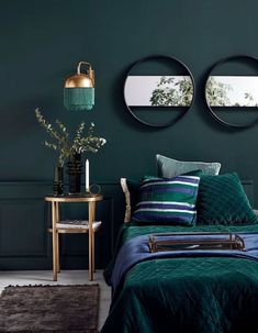 a bedroom with green walls and blue bedspread, gold side table and mirror on the wall