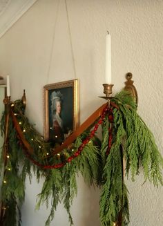 a christmas garland hanging on the wall next to a candle holder with a portrait in it