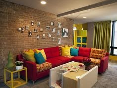 a living room with red couches and yellow curtains on the windowsill in front of a brick wall