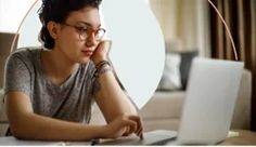 a woman sitting at a table with a laptop computer in front of her and an image of a round object behind her