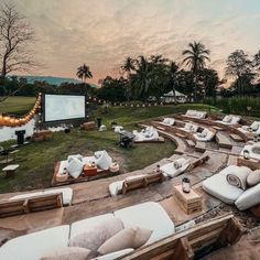 an outdoor movie is set up in the middle of a grassy area with white couches and pillows