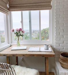 a table with a book, cup and pen on it in front of a window