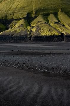 a large hill covered in green grass next to a sandy beach