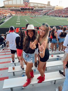 two girls giving the thumbs up sign in front of a football stadium full of people