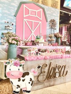 a pink and blue barn themed birthday party with farm animals on the wall, cow table cloths, flowers in vases, and cake stands