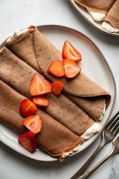 two crepes with whipped cream and strawberries are on a plate next to a fork