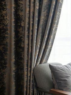 a couch sitting in front of a window covered in gray and gold curtains with floral designs