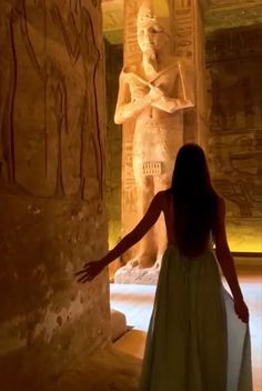 a woman in a green dress standing next to an egyptian statue