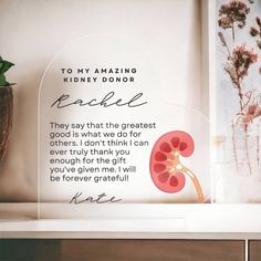 an acrylic sign on a shelf next to a potted plant and vase