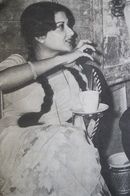 an old photo of a woman sitting at a table with a cup in her hand