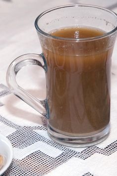 a glass mug filled with liquid sitting on top of a table next to a plate of food