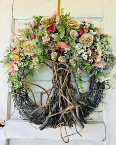 a wreath made out of branches and flowers hanging on the front door to decorate it