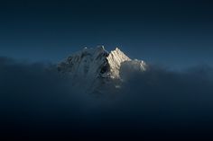 the top of a snow covered mountain is seen through some clouds in this dark blue sky