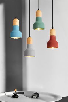 three different colored lights hanging from the ceiling above a white table with a black object on it