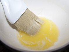 a wooden brush in a white bowl filled with yellow liquid