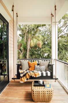 a porch swing with pillows on it and a coffee table in the middle next to it