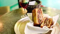 a plate with two sandwiches on it next to a glass of wine and a basket