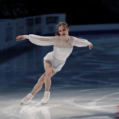 a woman skating on an ice rink wearing white clothes and holding her arms out in the air