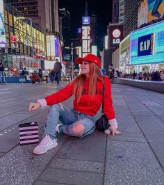 a woman sitting on the ground with her hand out and wearing a red shirt, jeans and sneakers