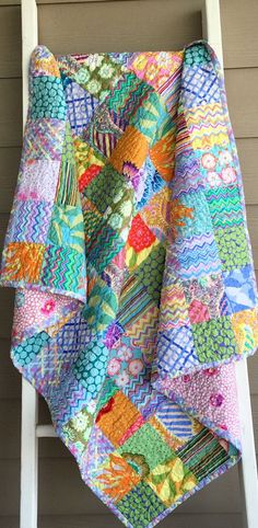 a multicolored quilt hanging from a white ladder on the side of a house