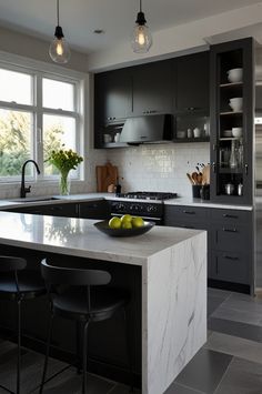 a kitchen with black cabinets and white marble counter tops, two yellow apples on the island