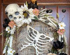 a wreath decorated with fake flowers and skeleton heads is displayed on a front door for halloween