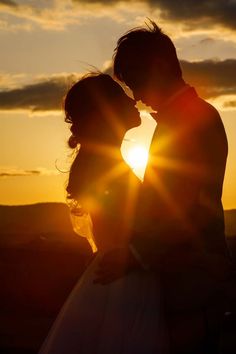 a bride and groom kissing in front of the sun