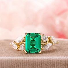 an emerald and diamond ring sitting on top of a cushioned surface with white diamonds around it