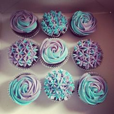 twelve cupcakes with blue and purple frosting in a box on a table