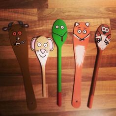 five wooden spoons with animal faces on them and one has a green plastic spoon in the middle